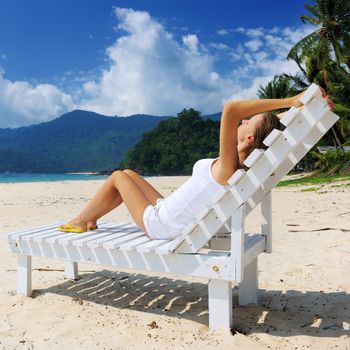 Girl on a tropical beach sitting at chaise lounge