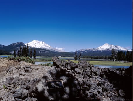 Two snow capped mountain peaks in the Cascade range next to lake and pine tree forest, Oregon