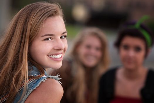 Smiling teenage girl with pair of female friends outdoors