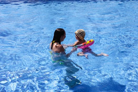 Mother teaching baby girl how to swim in a swimming pool.