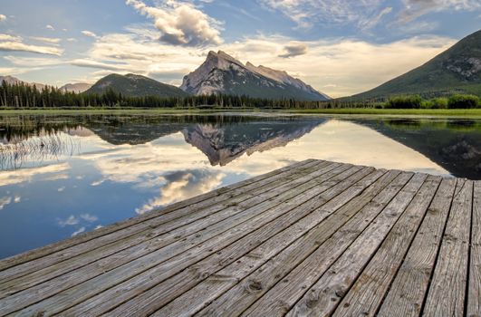 Wooden dock beside Vermilion lakes with perfect mountain reflection.