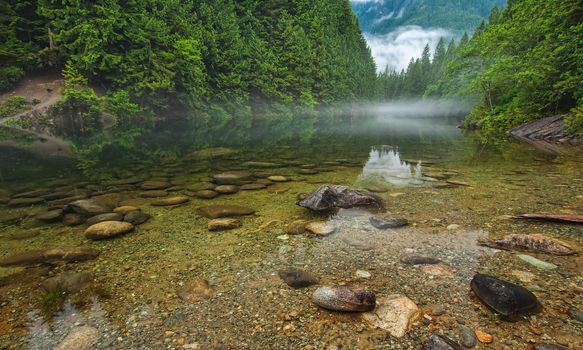 Very clear rock bottomed lake with misty clouds in the distance.