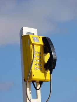 Photo of a yellow telephone isolated over a sky background