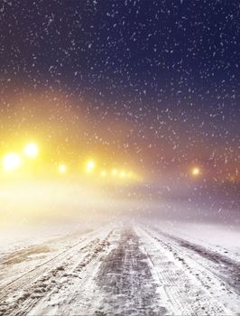 Snow covered winter road with shining streetlights at night