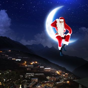 photo of santa claus sitting on the moon with a city and mountains below