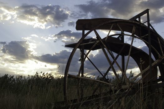 old farm equipment in field with clouds and bright sunset