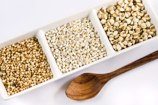  job's tears , barley and millet grains on white bowl and wooden spoon