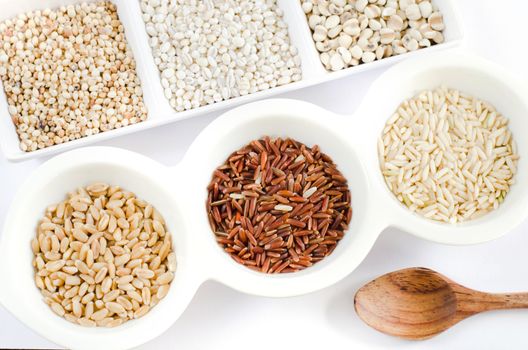 top views of grain and wooden spoon ,  rice , red rice , wheat,  job's tears , barley and millet grains on white bowl