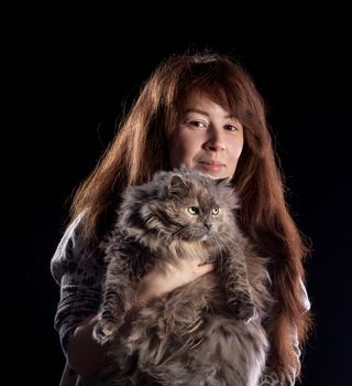 Young beautiful smiling woman holds fluffy cat, on black background