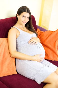 Gorgeous pregnant woman sitting on couch at home