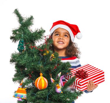 Smiling little mullato girl in Santa's hat with gift box and and christmas pine, isolated on white