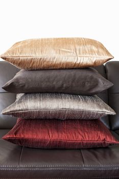 Four colorful cushions stacked on dark brown leather couch