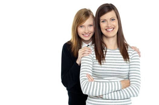 Smiling mother standing with her hands crossed and daughter embracing her from behind.