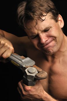 Muscular shirtless man struggles to loosen a big nut with a pipe wrench