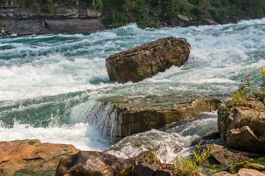 Rock stands against the force of intense white-water rapids in the Niagara river.