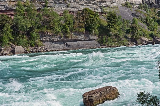 Rock stands against the force of intense white-water rapids in the Niagara river.