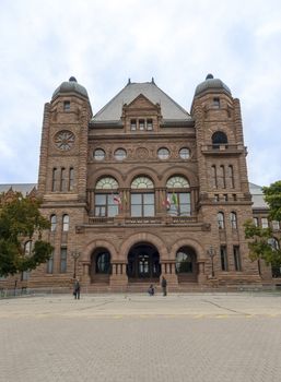 Toronto, Ontario, Canada - July 10, 2012: People in Queens Park beside the ornate Romanesque facade of the Legislative Assembly of Ontario building and the Canadian flags flying high.
