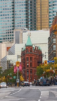 Toronto, Canada - October 07, 2012: Toronto’s landmark Flatiron Building, a restored late 19th century Victorian office building built by architect David Roberts Jr. In the background on the left, the two towers . Picture is taken in  the afternoon, while cars are moving along  Front Street East. Trees on the right start to change their colours from green to yellow. 