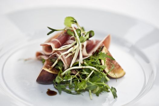 A portion of sliced serrano with salad, sprout and sliced fig 