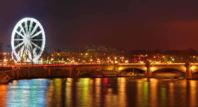 Image of the illuminated Ferry Wheel located in Place de la Concorde and colorful light reflections in the river Seine in Paris.