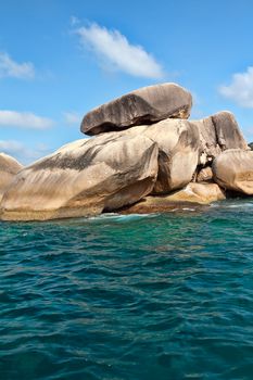 Rocks in the azure sea against the blue sky with clouds