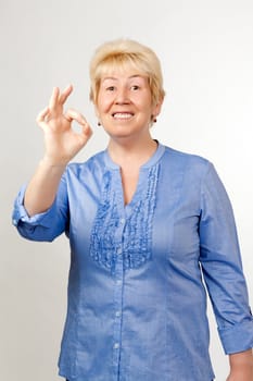 Middle-aged woman shows OK, on grey dackground