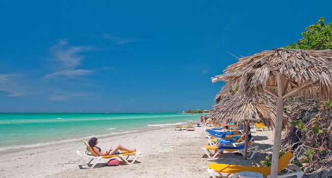 Line of beach chairs on the beach looking out to a greean and blue ocean horizon