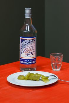 a bottle of vodka "White Sea" pickles and a glass on a table with red tablecloth