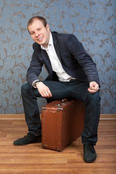 casual man sitting on an old brown retro suitcase