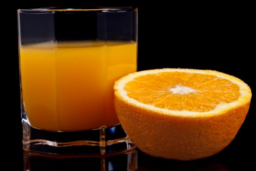 glass of orange juice and half of the orange on black background
