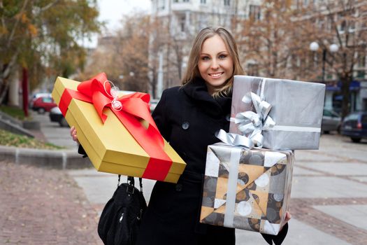 Beautiful smiling woman in the street holding presents, looking at camera