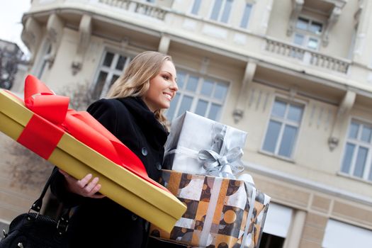 Smiling blonde female walking in the street, carrying Christmas gifts in both hands