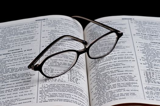 Open bible and the glasses on black background