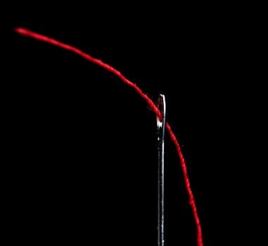 Needle and red thread on black background