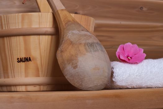 white towel with flower on top next to bucket with ladle in a wooden sauna