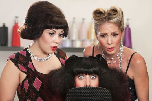 Wide eyed woman behind mirror with two friends in hair salon