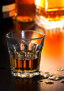 Glass of whiskey on table with drops, shallow DOF