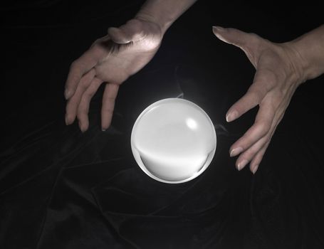 high angle shot of a glowing crystal ball surrounded by black crinkly fabrics and two hands around