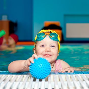 Little girl playing with blue ball in a swimming pool