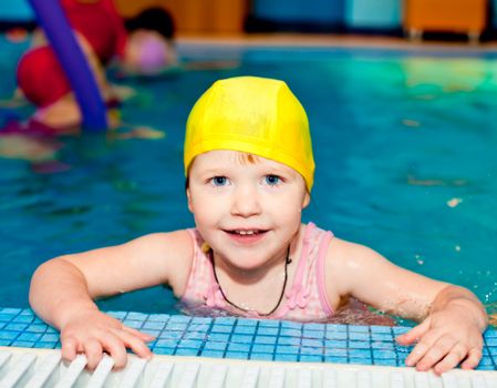 Happy cute little girl wearing yellow swimming cap in a pool