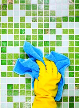 Hand in yellow protective glove cleaning mosaic wall