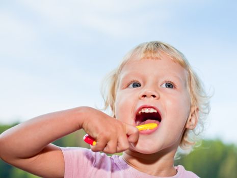 Portrait of cute little girl brushing teeth outdoors