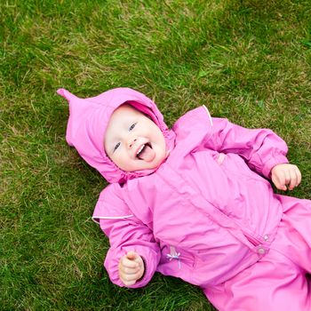 Cute little baby girl wearing pink suit lying on lawn outdoors