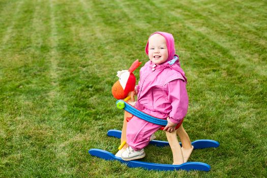 Cute little baby girl wearing pink suit sitting on rocking horse outdoors