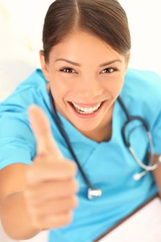 Nurse happy thumbs up smile. Closeup high angle view portrait of young medical professional nurse or doctor excited. Multiracial Asian / Caucasian female model in her twenties.