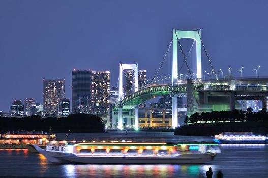 very famous Tokyo landmark, Tokyo Rainbow Bridge over bay waters with scenic night illumination and traditional Japanese boats and human silhouette
