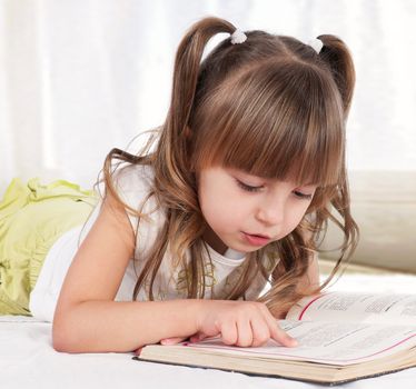 Lovely little girl, reading a book, on the bed