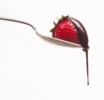A piece of fruit in a spoon with chocolatte dropping in