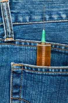Medical syringe with yellow liquid in a blue jeans rear pocket