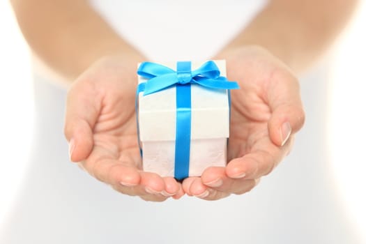 Decorative gift box tied with a turquoise ribbon and bow carefully cupped in female hands as she gives a surprise present to a loved one
